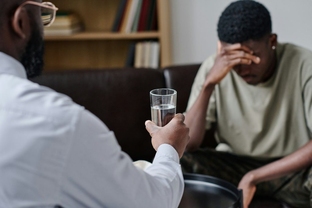 Psychothérapeute africain donnant un verre d'eau pour soutenir le patient au bureau pendant une séance de psychothérapie