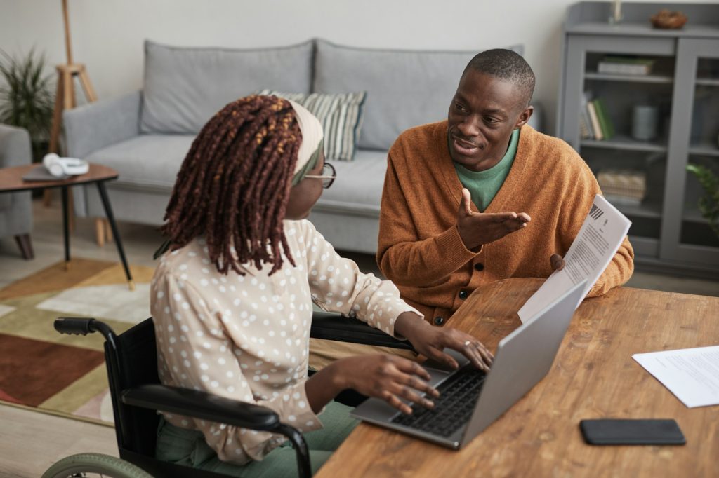 Portrait d'une jeune femme afro-américaine utilisant un fauteuil roulant travaillant à domicile avec un mari attentionné l'aidant à copier son espace