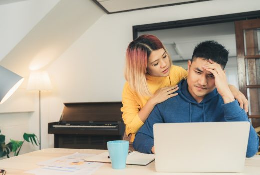 Jeune couple asiatique stressé gérant ses finances, examinant ses comptes bancaires à l'aide d'un ordinateur portable et d'une calculatrice dans une maison moderne.