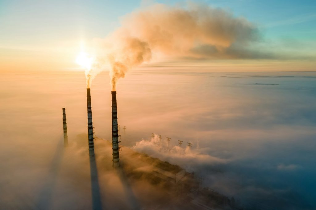 Vue aérienne des tuyaux hauts d'une centrale électrique au charbon avec de la fumée noire remontant une atmosphère polluante au coucher du soleil.