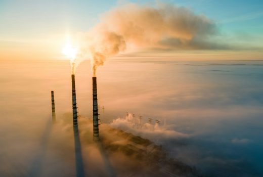 Vue aérienne des tuyaux hauts d'une centrale électrique au charbon avec de la fumée noire remontant une atmosphère polluante au coucher du soleil.
