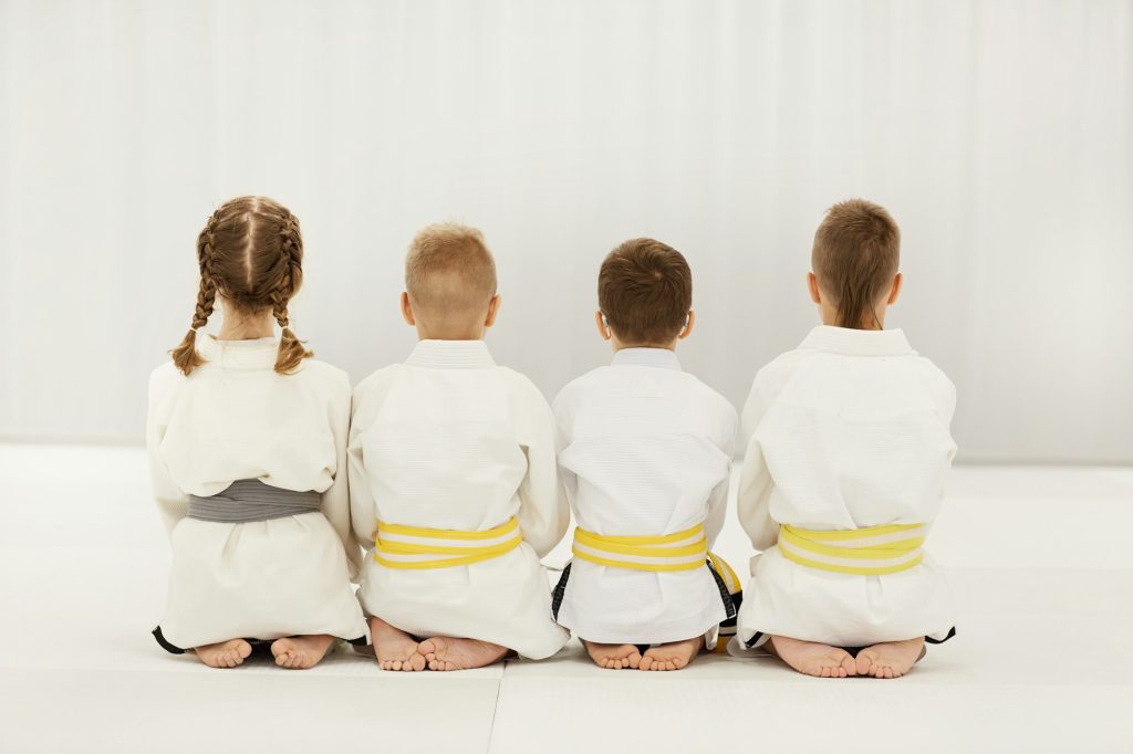 Vue arrière d'enfants pieds nus en kimono blanc assis sur le sol ensemble dans une rangée