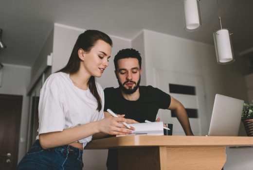 Faible angle de couple sérieux dans des vêtements décontractés assis à une table en bois avec un ordinateur portable et prenant des notes tout en travaillant ensemble