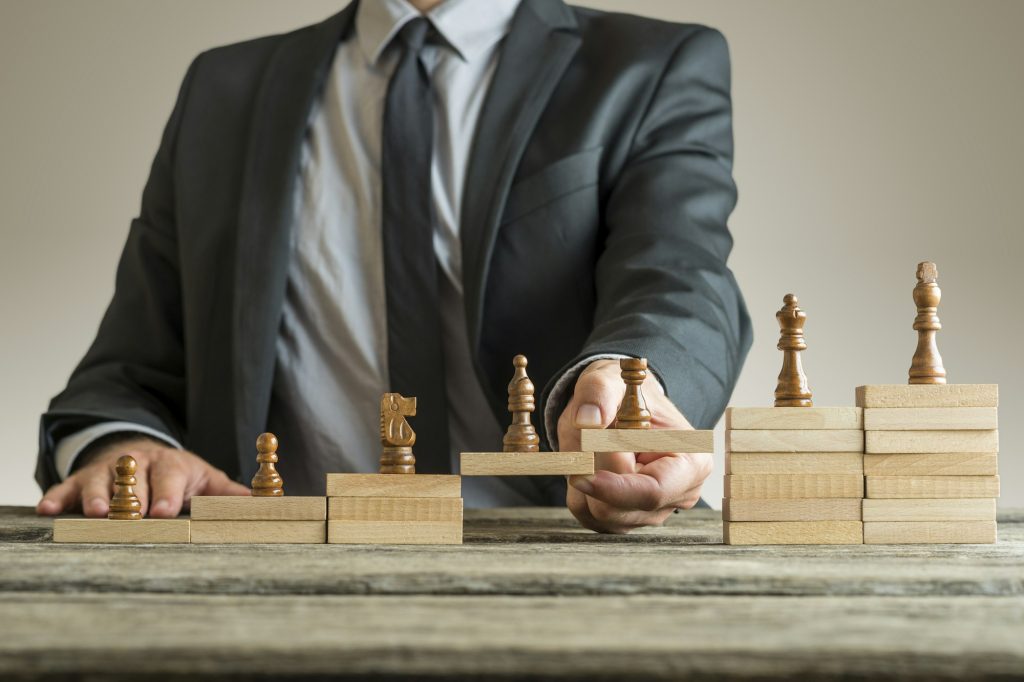 Image conceptuelle de la gestion de carrière avec un homme d'affaires formant un pont de blocs de construction en bois pour les pièces d'échecs se développant du pion au roi.