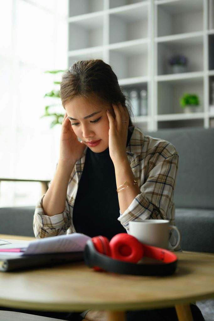 Jeune femme stressée tenant la tête dans les mains, gérant les finances du ménage frustrée par les problèmes financiers familiaux.