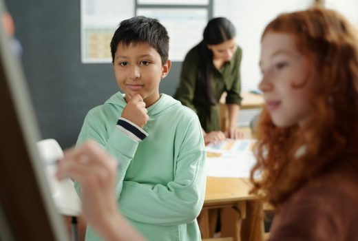 Concentrez-vous sur un écolier pensif regardant les règles de grammaire sur un tableau blanc tout en se tenant à côté d'un camarade de classe écrivant des formes de verbes irréguliers à la leçon
