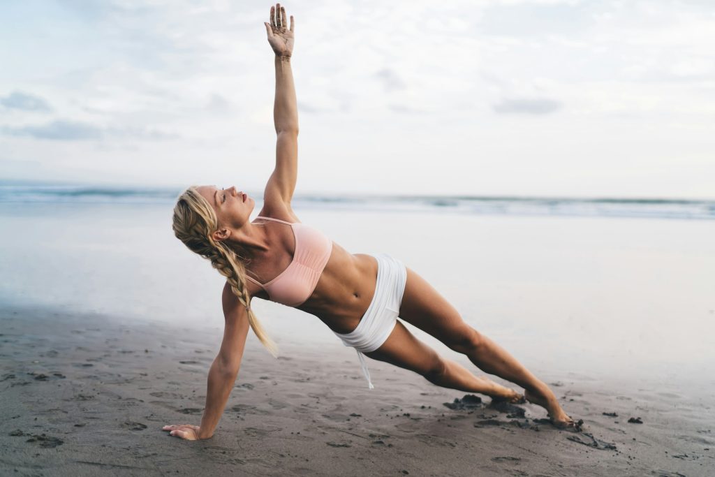 Vue sur toute la longueur, femme caucasienne au corps sportif faisant des exercices d'étirement au bord de la mer tout en s'entraînant à l'extérieur.