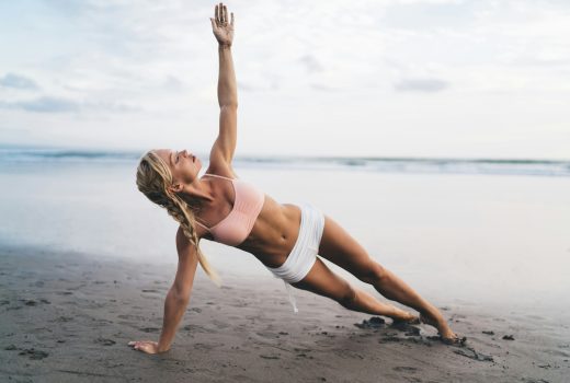 Vue sur toute la longueur, femme caucasienne au corps sportif faisant des exercices d'étirement au bord de la mer tout en s'entraînant à l'extérieur.