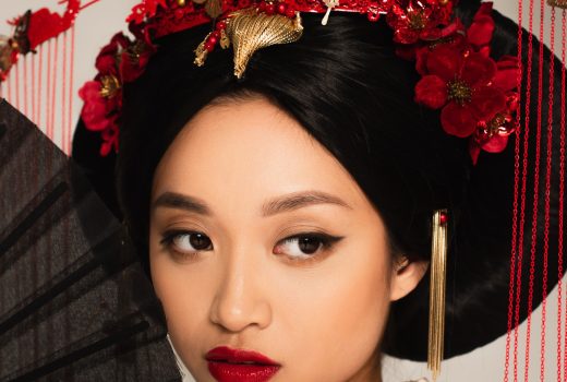 Femme asiatique avec une coiffure nationale regardant loin près d'un ventilateur isolé sur gris