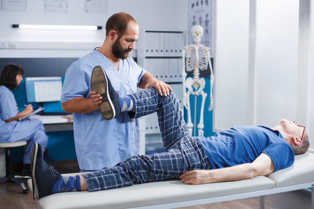 Le physiothérapeute effectue des exercices de jambe pour étirer les muscles et casser les os d'un homme âgé dans un cabinet d'hôpital.