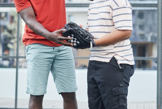Père afro-américain positif en t-shirt rouge montrant comment attraper la balle tout en expliquant les règles du baseball à son fils