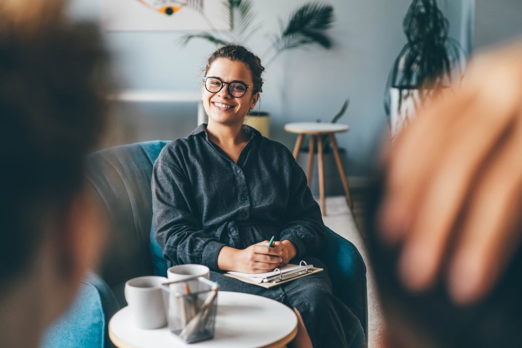 Un couple familial d'âge moyen discute de problèmes relationnels avec un psychothérapeute qualifié à une petite table basse dans un bureau de clinique légère