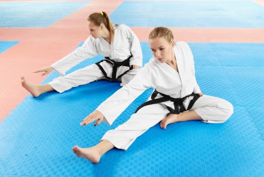 Les femmes sportives portant des ceintures de kimono et noires blanches, s'étendant avant l'entraînement dur en classe de combat.