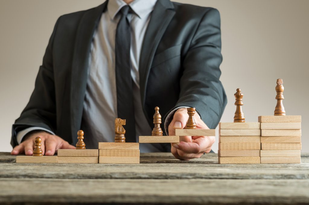 Image conceptuelle de la gestion de carrière avec un homme d'affaires formant un pont de blocs de construction en bois pour les pièces d'échecs se développant du pion au roi.