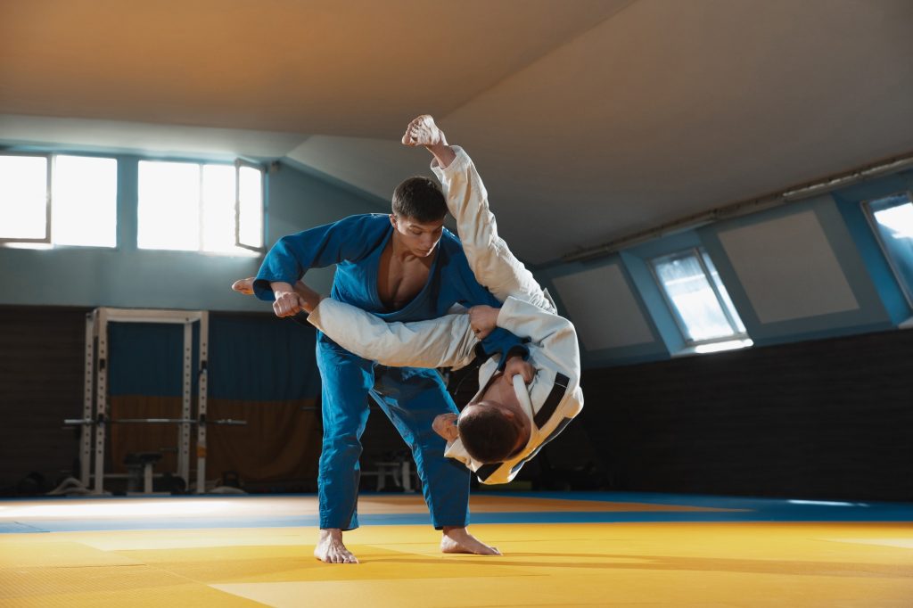 Deux jeunes combattants de race blanche de judo en kimono blanc et bleu avec des ceintures noires entraînant des arts martiaux au gymnase avec expression, en action, mouvement.