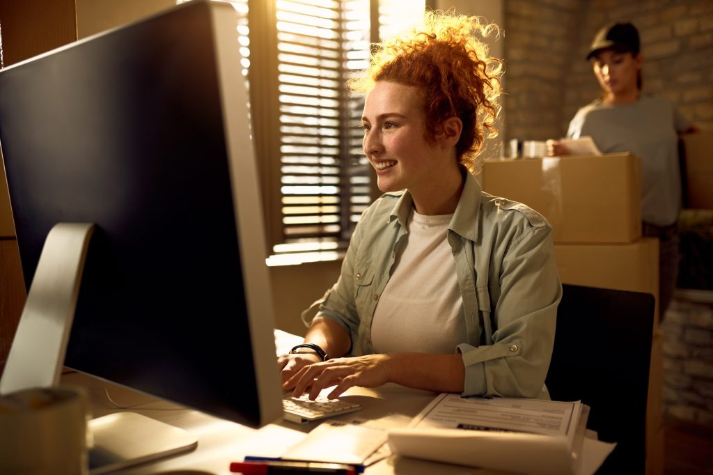 Jeune femme heureuse qui utilise un ordinateur tout en écrivant un e-mail et en travaillant au bureau de Courier.